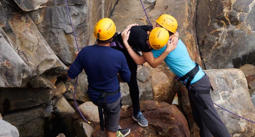 Two people wearing yellow helmets embrace while another looks on. 